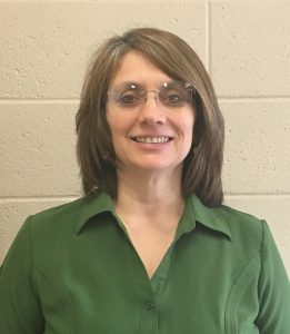 A woman with shoulder'length brown hair and glasses, wearing a green blouse smiles.