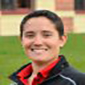 A woman with short dark hair smiling. She is wearing a red collared shirt with a black jacket.