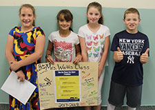 Four young students hold their class's No Place For Hate poster, which is signed by all. The boy on the right is giving two thumbs up.