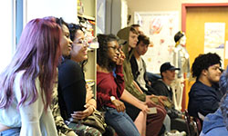 A large group of students, some sitting on the windowsill, listen as the Army recruiter discusses team building.