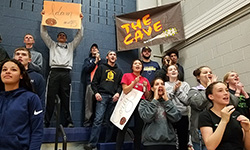 Students in the stands support their Unified team, clapping and holding posters.