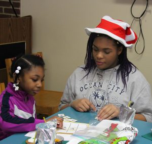 One of the high school student volunteers. wearing a red and white striped hat, helps one of the kindergarten children with a matching game.