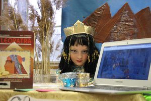 Young girl with dark hair and a gold crown and jewels tells the story of Cleopatra