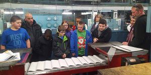Several members of the Crispell Middle School Life Skills class watch as newspapers roll off the press at the Times Herald-Record facility.