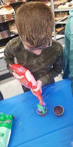 A middle school boy squeazes icing from a tube onto a cupcake.