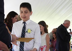 A fifth grade boy in white shirt and tie accepts his certificate and shakes hands