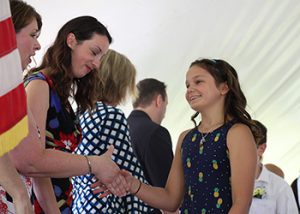 A fith grade girl in a blue print dress shakes hands with a teacher