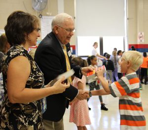 Third grade boy in a striped shirt shakes hands with a Rotary official and accepts his dictionary.