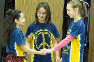 Two fifth grade girls face each other and hold hands while another is in between mediating.