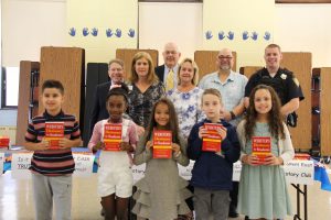 Five third graders hold red dictionaries while six adults stand behind them.