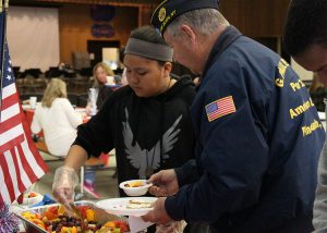 A student spoons out fresh fruit to a veteran.
