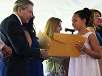 A girl in a pink dress accepts her certificate from superintendent