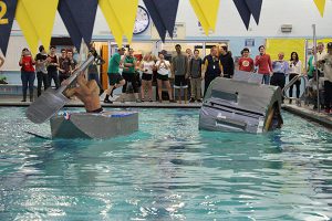 One boy paddling a boat and another boat in the shape of a hamster wheel in the pool.