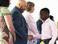 A fifth grade boy with a button down shirt shakes the hand of an administrator