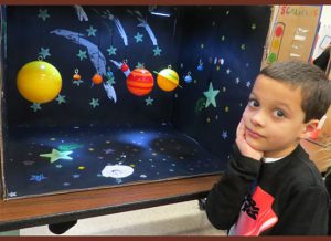 A small boy with his head resting on his hand and a colorful solar system in the background.