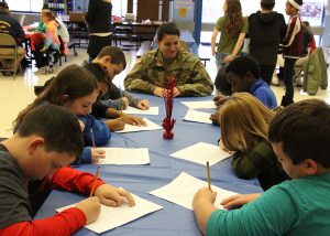 Circleville Middle School teacher Nina LaConte in her reserves uniform talks to a table filled with students who are writing down what she says.