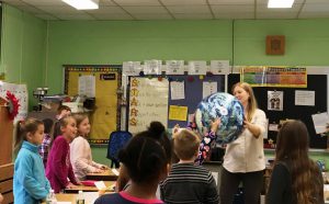 Teacher holds a large globe up for the students to see