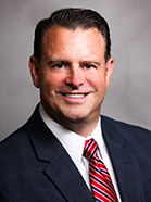 headshot of man with red striped tie and dark suit, smiling