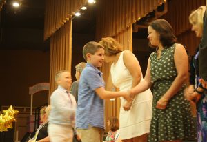 A boy wearing a blue shirt shakes hands with a district board member