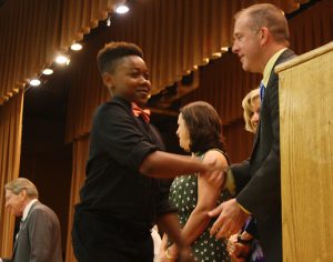 Fifth grader wearing a red bow tie shakes hands with his principal