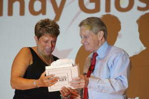 Woman in back shirt accepts award from superintendent in blue shirt and red tie