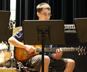 Student with glasses sitting and playing an electric guitar