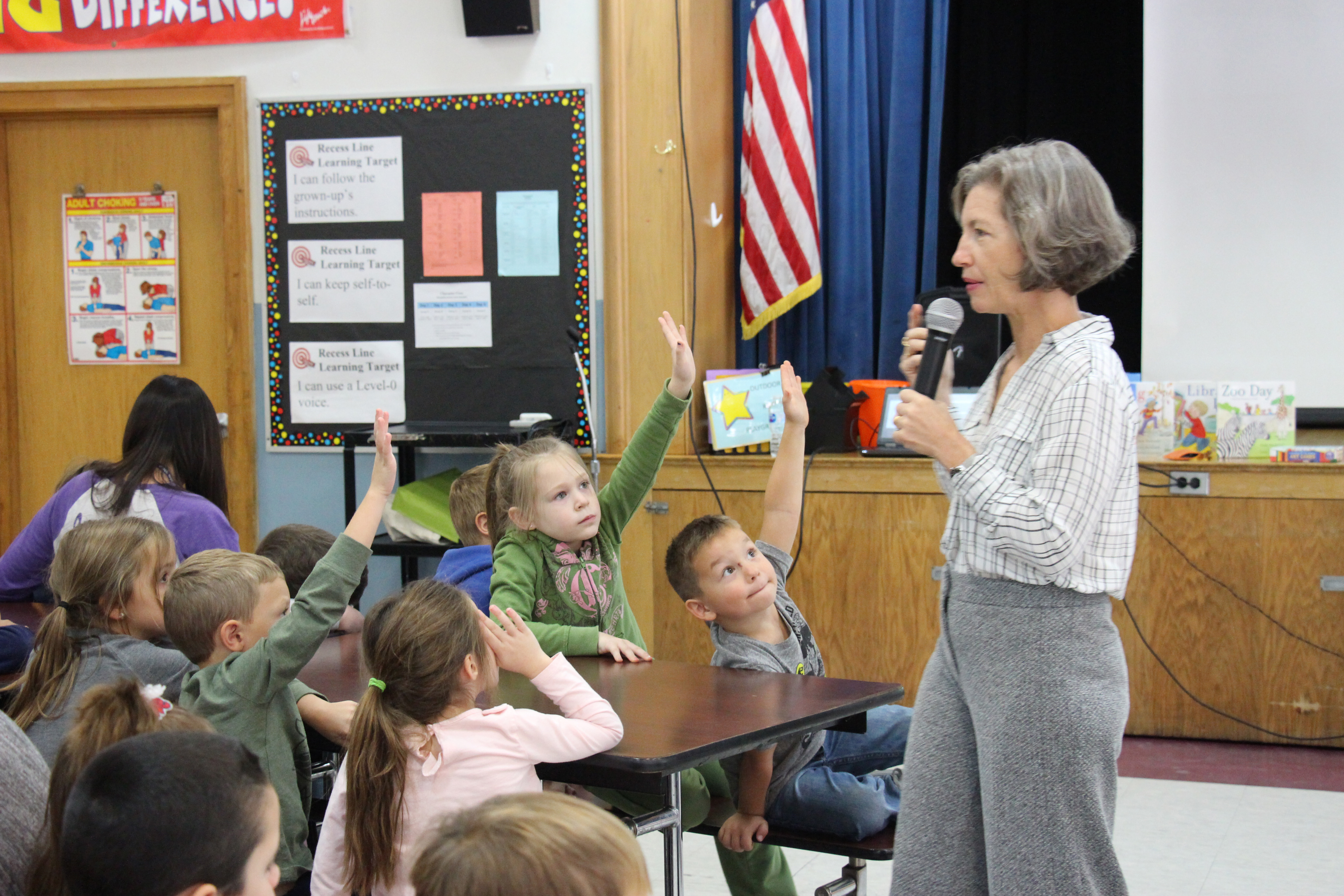 Students raise their hands wanting to be called on by woman with microphone, short gray hair.