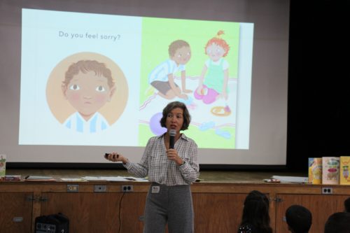 Large screen in background shows illustrations created by author standing in front of it.