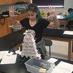 sixth grade girl with her hands up showing she finished her index card tower with a stuffed animal on top