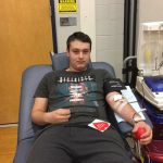A high school boy is lying on a bed donating blood