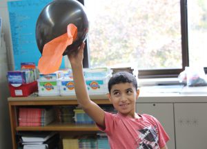 Boy in red t shirt holding up his black balloon with a piece of crepe paper attached to it