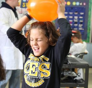 Girl with black t shirt on rubs an orange balloon on her head to cause static electricity