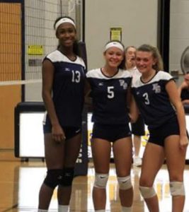 Three girls in volleyball uniforms near a volleyball net