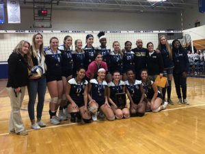 High school girls in blue volleyball uniforms stand and kneel in two rows 