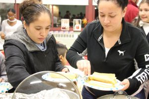 Two women wearing black getting food out of a pot