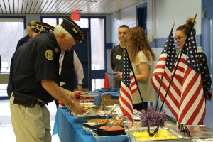 A veteran takes breakfast foods from the table, which also has American flags on it