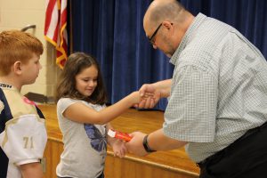 Man from Rotary with glasses shakes hands with a third grade girl and hands her the dictionary