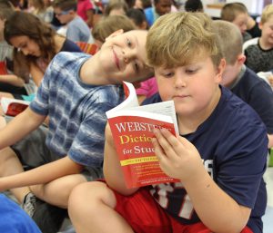 Boy in blue shirt reading his Websters dictionary with another boy sitting next to him leaning in and smiling
