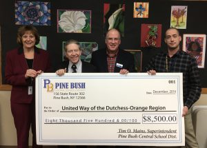 Four people holding an oversized check in the amount of $8,500 made out to the United Way from Pine Bush Schools.