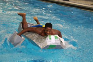 A high school student in a bathing suit paddles on his boat