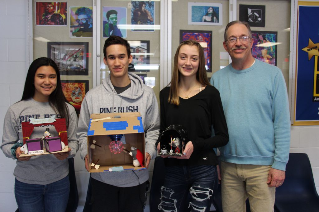 Three high school students, two girls and one boy, hold their winning moles. With them is their chemistry teacher