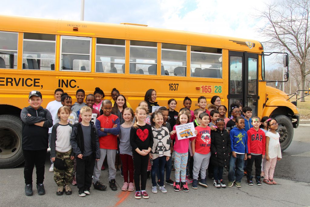 A bus load of elementary students stand alongside of their bus with their bus driver after being named Boss Bus for the month of February