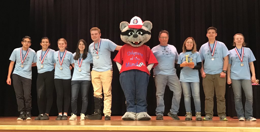 Seven high school students and their two coaches are on stage with the Odyssey of the Mind mascot.