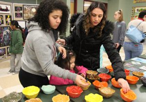 Two women choose from many student-made bowls which are many colors