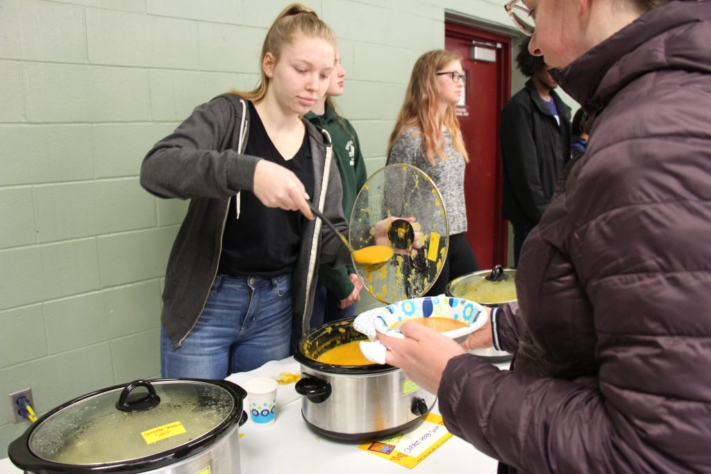 Young woman ladels soup into a paper bowl held by an attendee