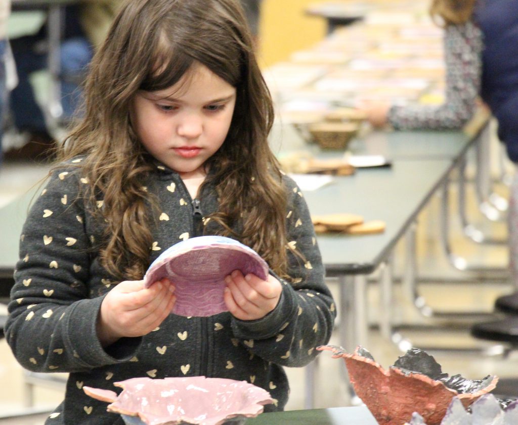 Young girl with long dark hair holds one of the handmade bowls and looks very intently at it.