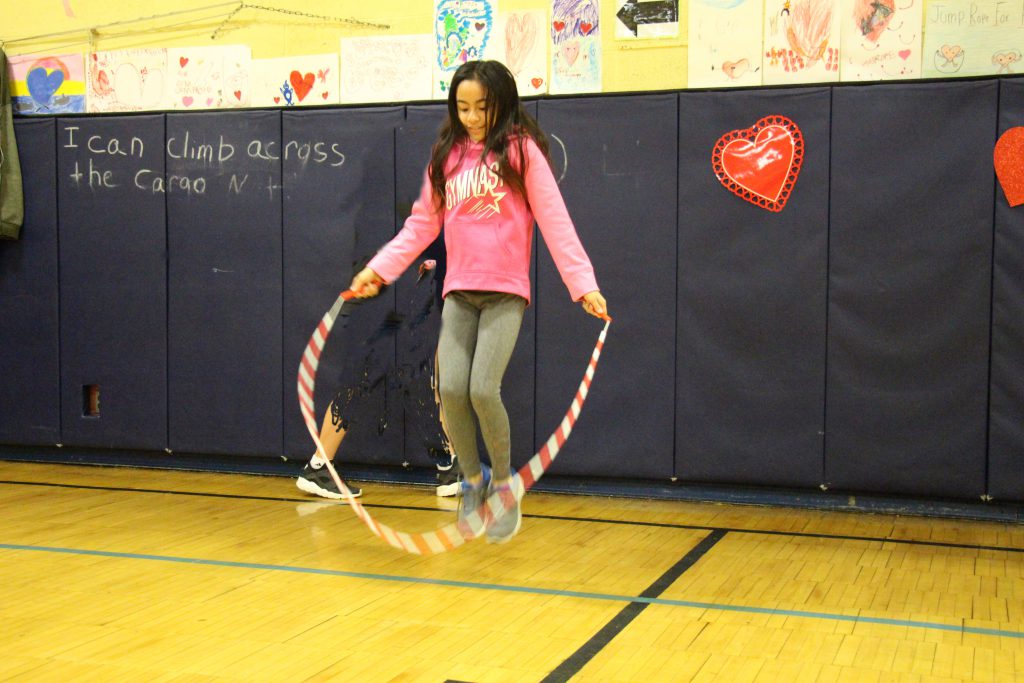 Elementary student dressed in pink shirt jumps rope in the gym.