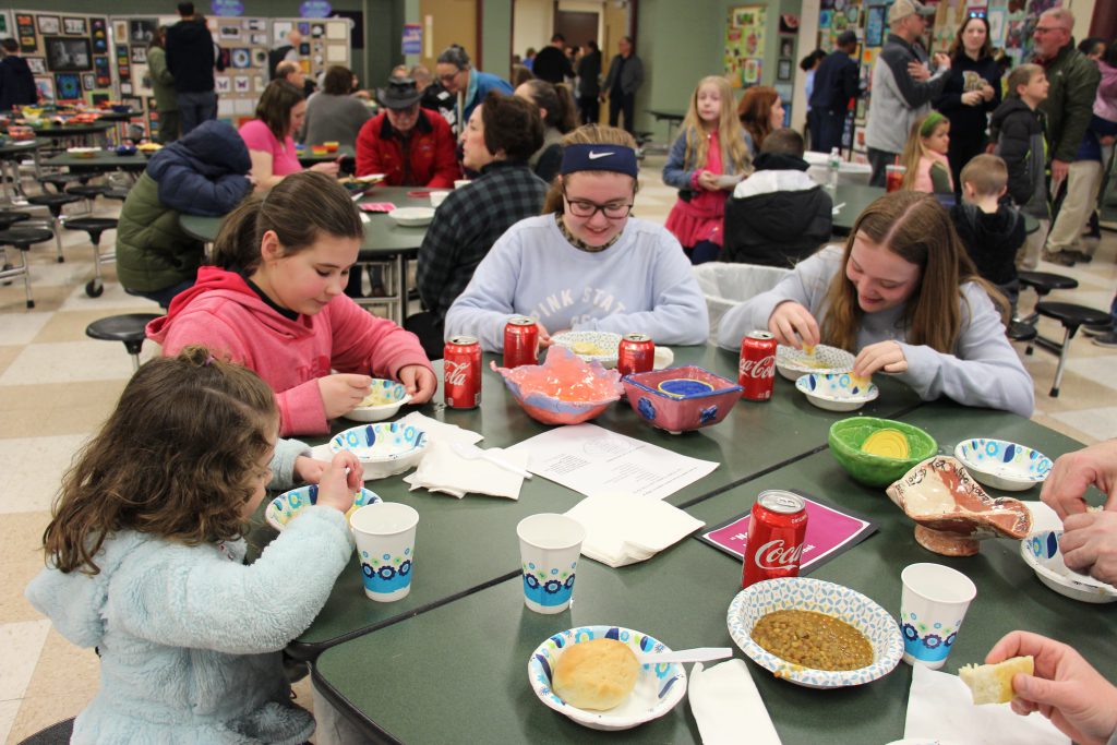 Four girls sit at a round table eating soupl