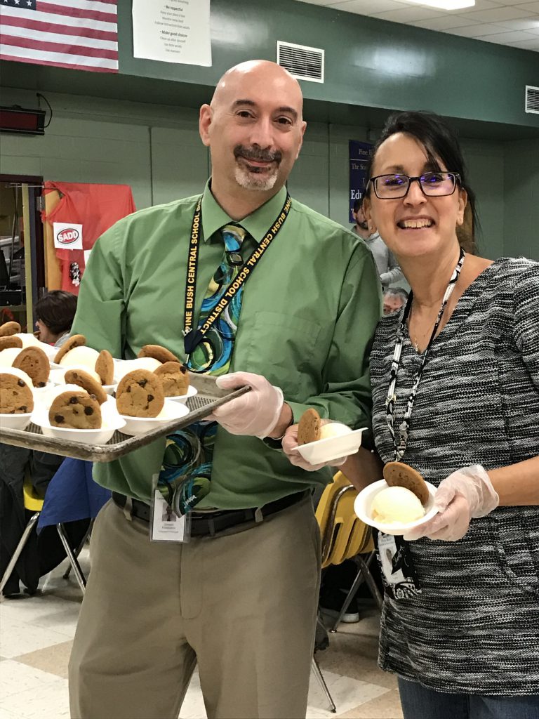 A man in a green shirt and tie holding a tray of vanilla ice cream and cookies and a woman in a black striped shirt holding bowls of ice cream and cookies