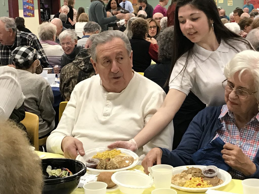 Student serving turkey dinner to a senior citizen